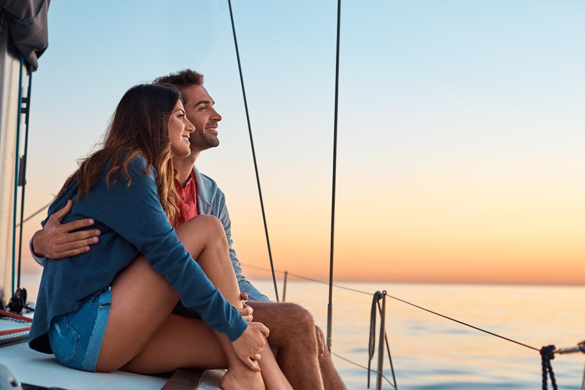 Couple hugging, watching a sunset on their sailboat.